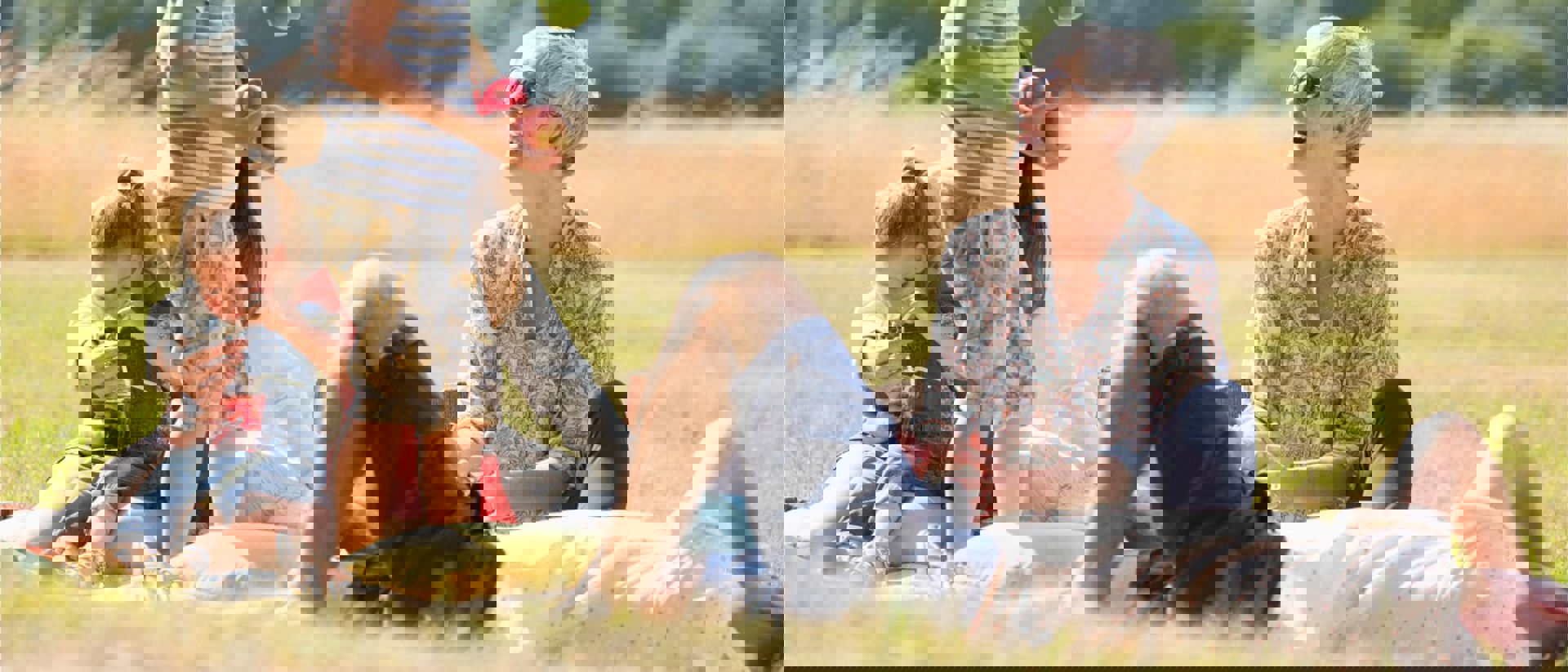 Multi-generational family has a picnic in a park while the grandmother watches a young boy juggle apples.